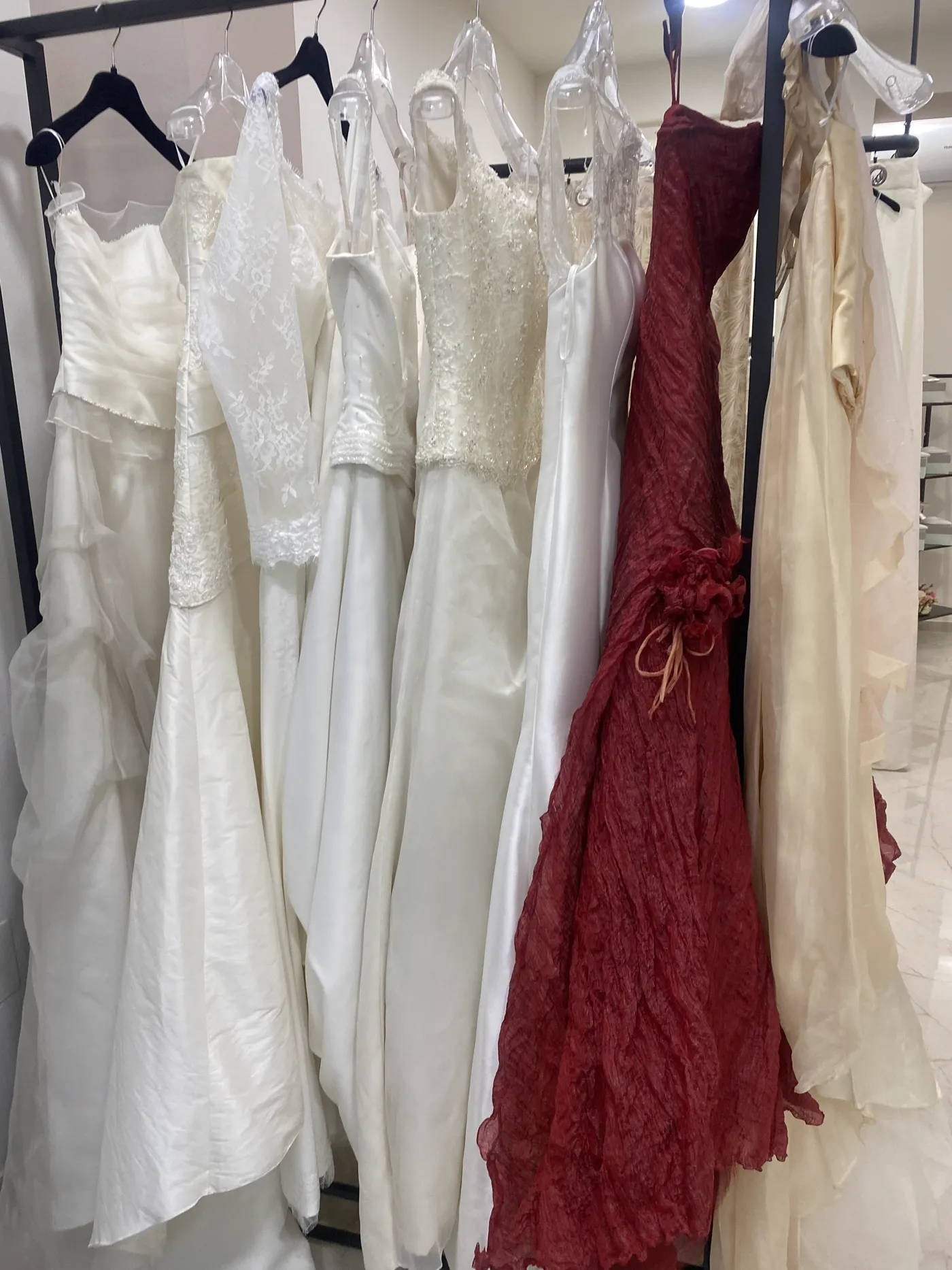 Collezione di abiti da sposa esposti nel negozio: pizzo, raso, panna, con un abito rosso passione tra i bianchi